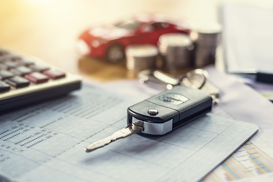 Car key, money, and calculator laying on car loan paperwork.